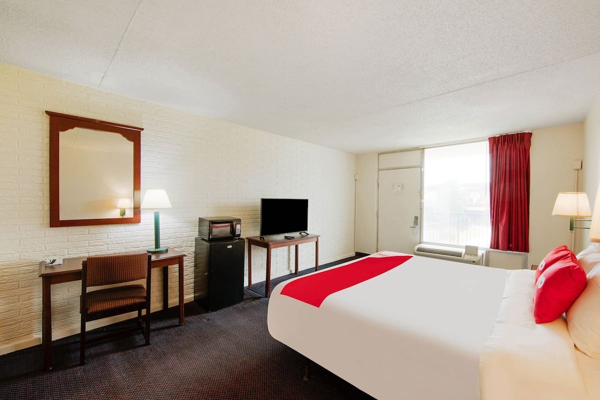 Une chambre d’hôtel comprenant un lit, un bureau avec une télévision, un miroir, une fenêtre avec des rideaux et une porte.
