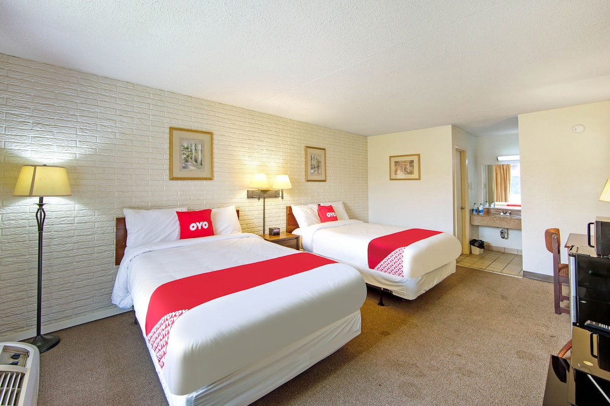 Une chambre d’hôtel avec deux lits, un bureau, une chaise, une télévision et une salle de bain visible à travers une porte ouverte.