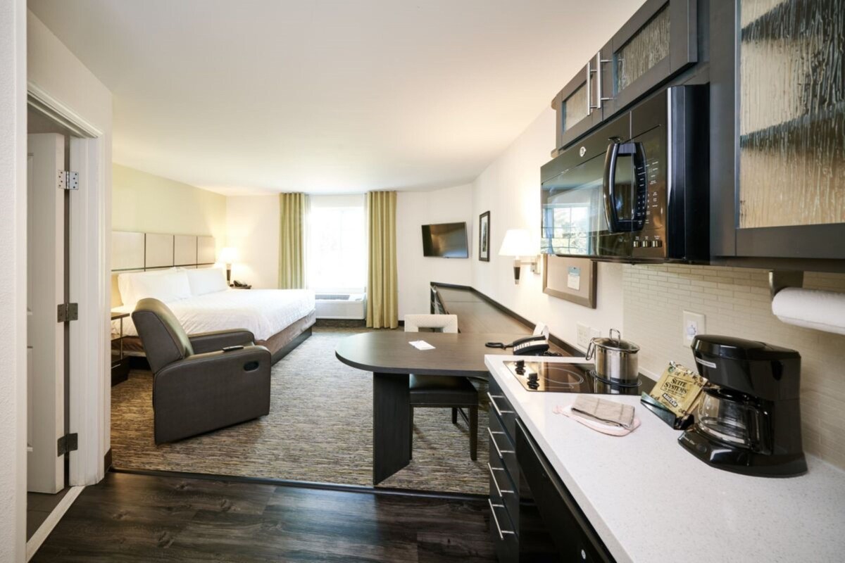 Een hotelkamer met een bed, een bank, een eettafel, een keukenhoek met een magnetron en een koffiezetapparaat.