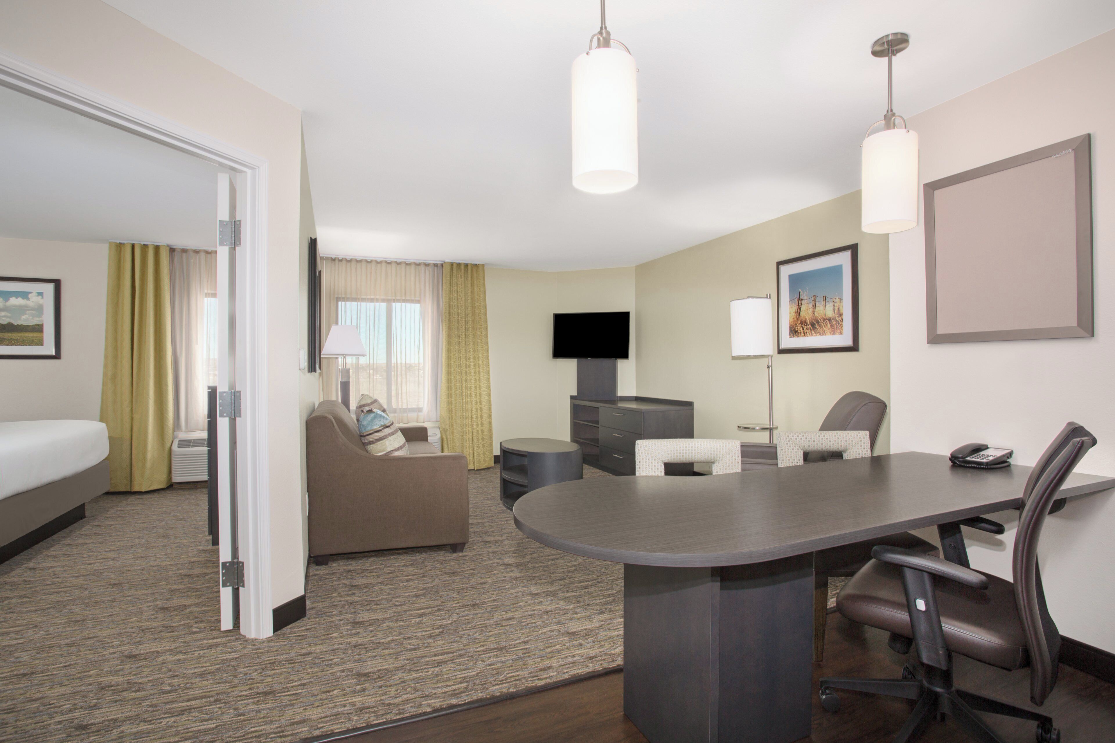 A hotel room with a bed, a sofa, a desk with a chair, a television, and a lamp.