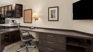 Hotelkamer met kitchenette, bureau, stoel, flatscreen-tv, lamp en lijstjes met afbeeldingen aan de muur.