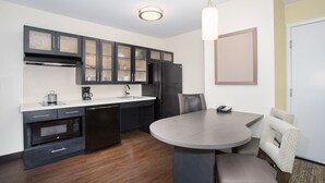 Een moderne keuken met donkere kastjes, een ingebouwde magnetron en een eethoek met een ronde tafel en stoelen.