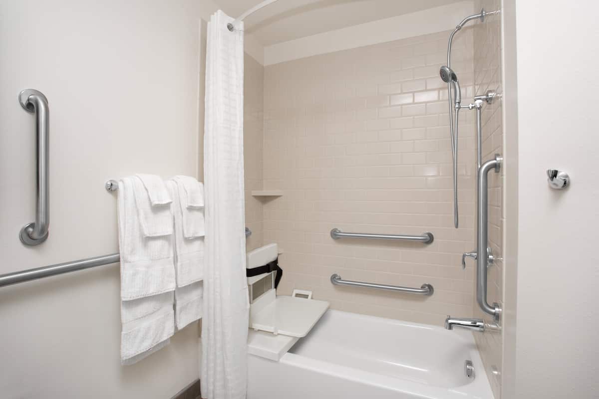 Une salle de bain avec une baignoire blanche, des barres d’appui, une douche avec un pommeau de douche amovible et un porte-serviettes blanc.