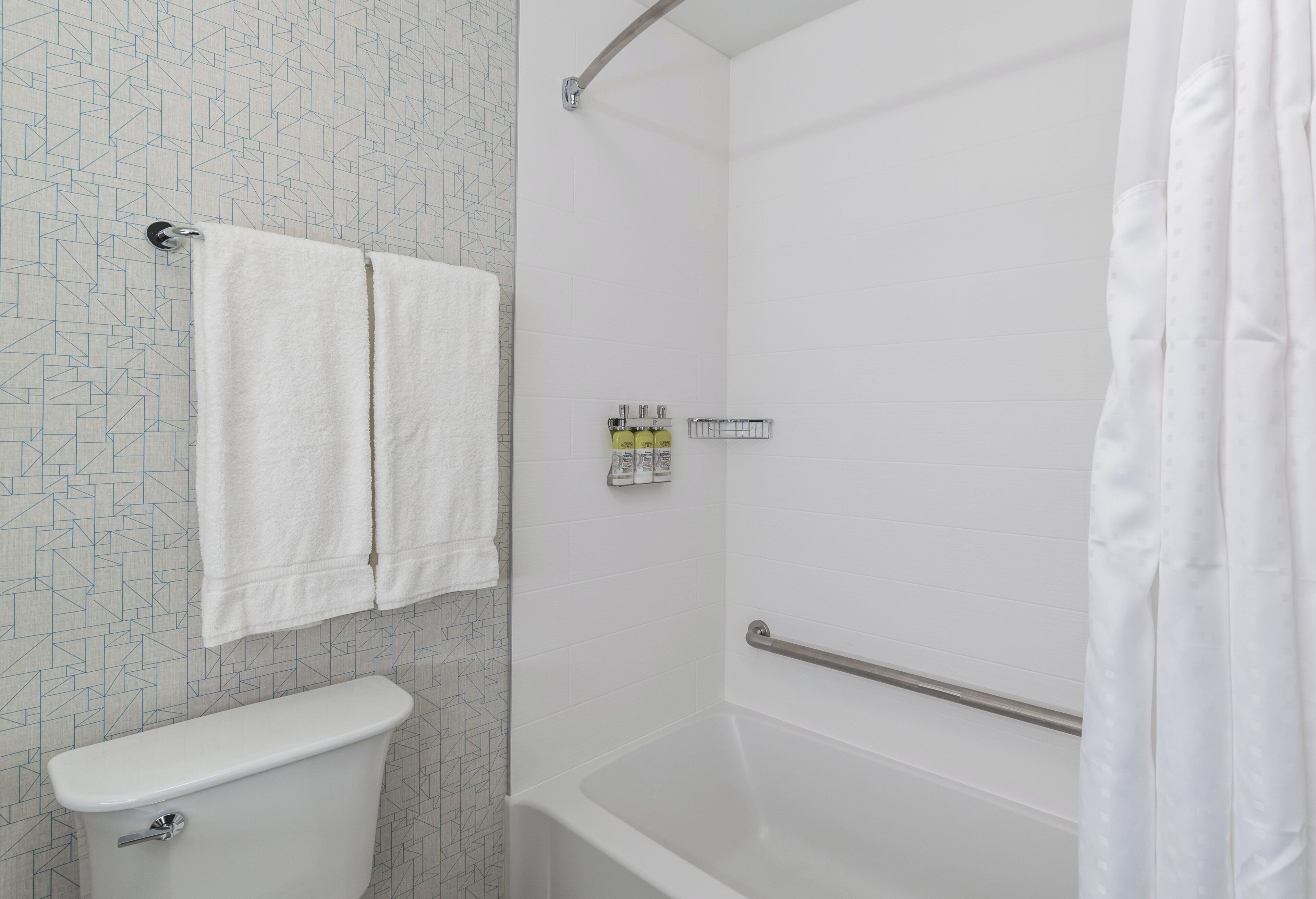 A bathroom with a toilet, a shower with a grab bar, and a towel rack.