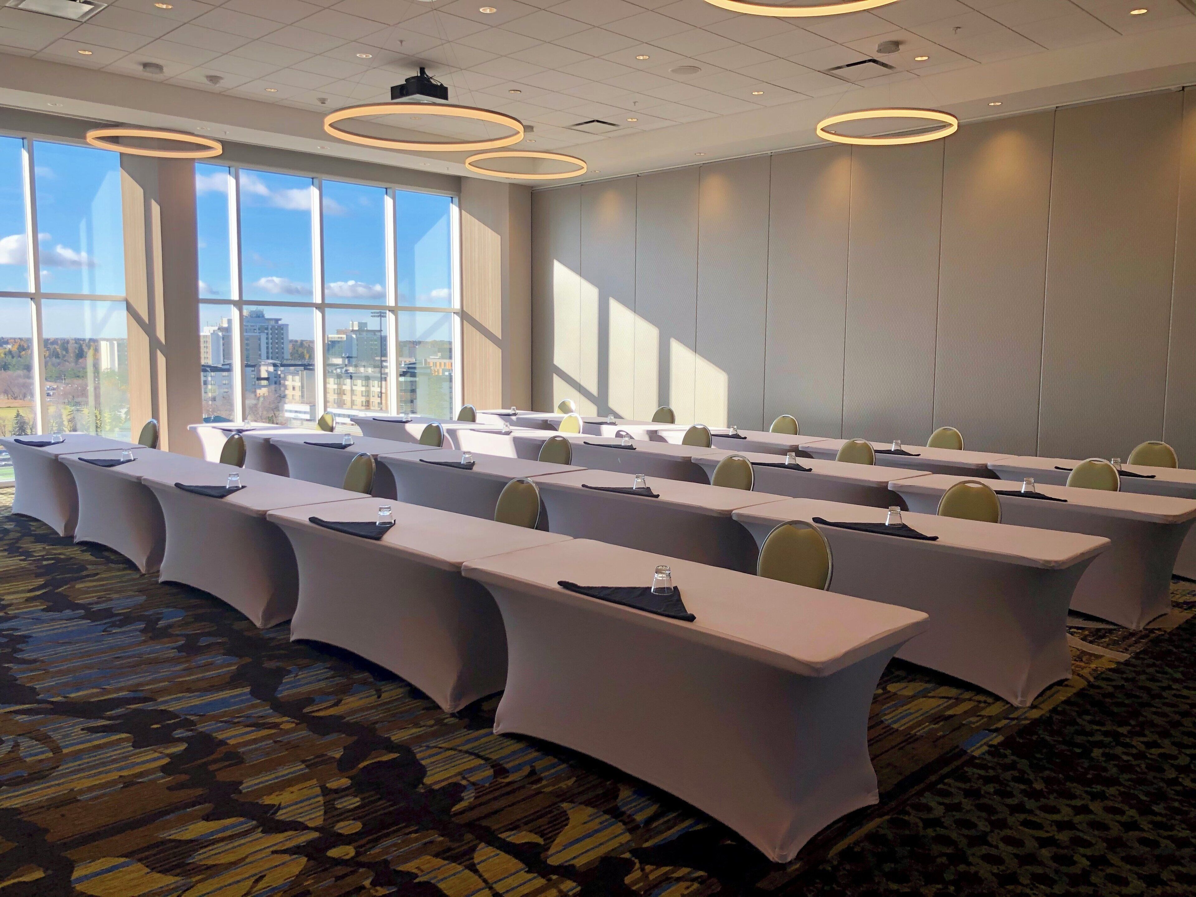 Une salle de conférence dotée de longues tables, de chaises et d’une grande fenêtre donnant sur le paysage urbain.