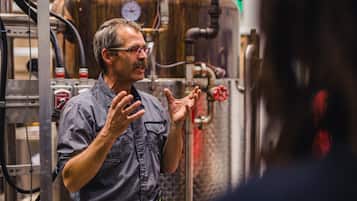 A man in a checkered shirt standing in front of industrial equipment, likely in a brewery or distillery.