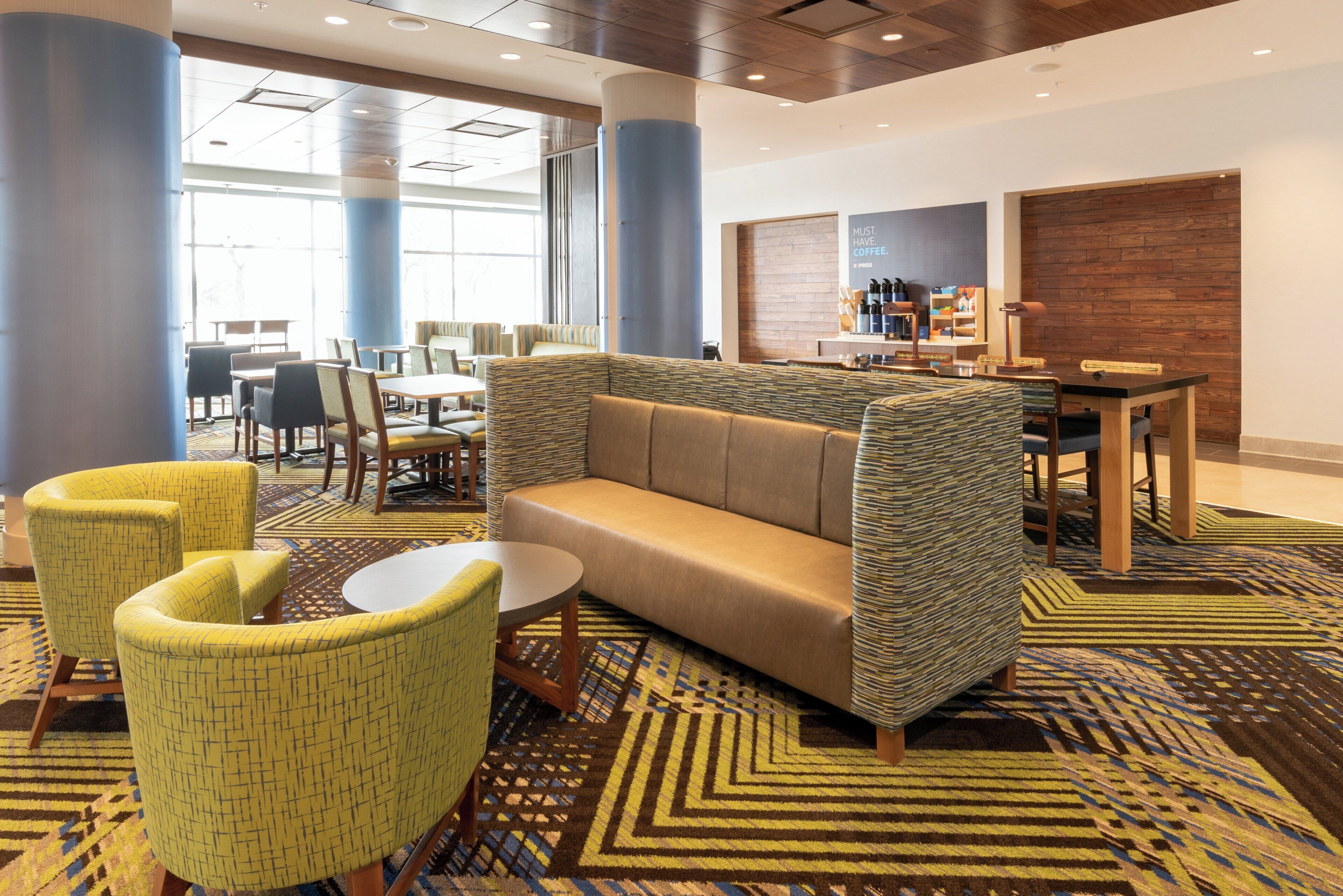 A hotel lobby with a sofa, chairs, a coffee station, and a patterned carpet.