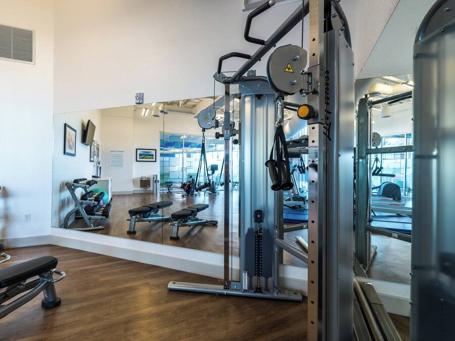 Un gimnasio con diferentes máquinas de ejercicio, un espejo grande y suelo de madera.