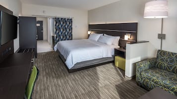 Quarto de hotel com cama, mesas de cabeceira, televisão, escrivaninha, cadeira e um sofá estampado.