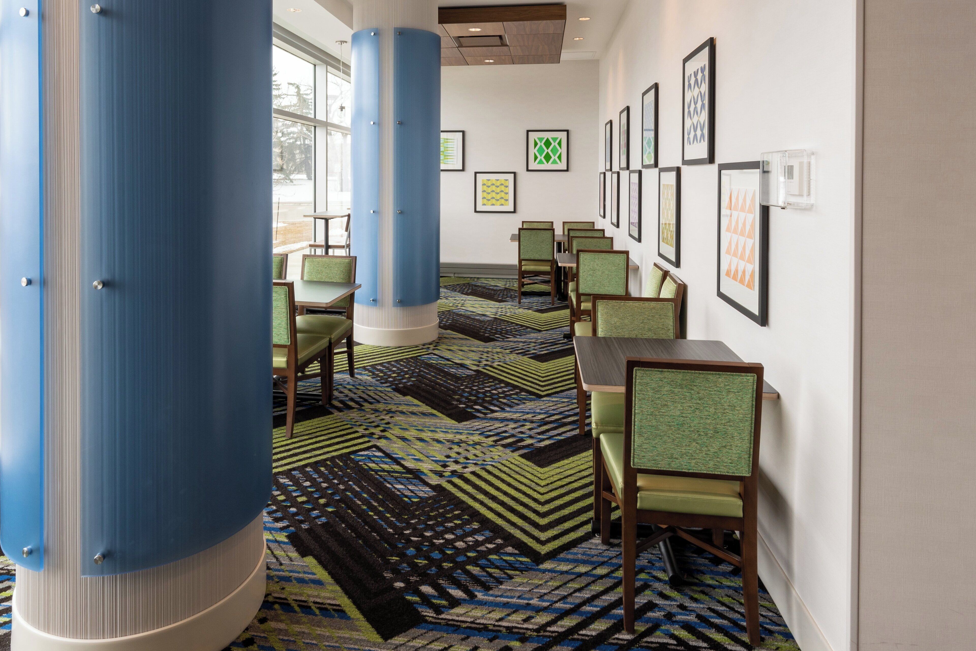 A hotel lobby with a patterned carpet, green upholstered chairs, and framed artwork on the walls.