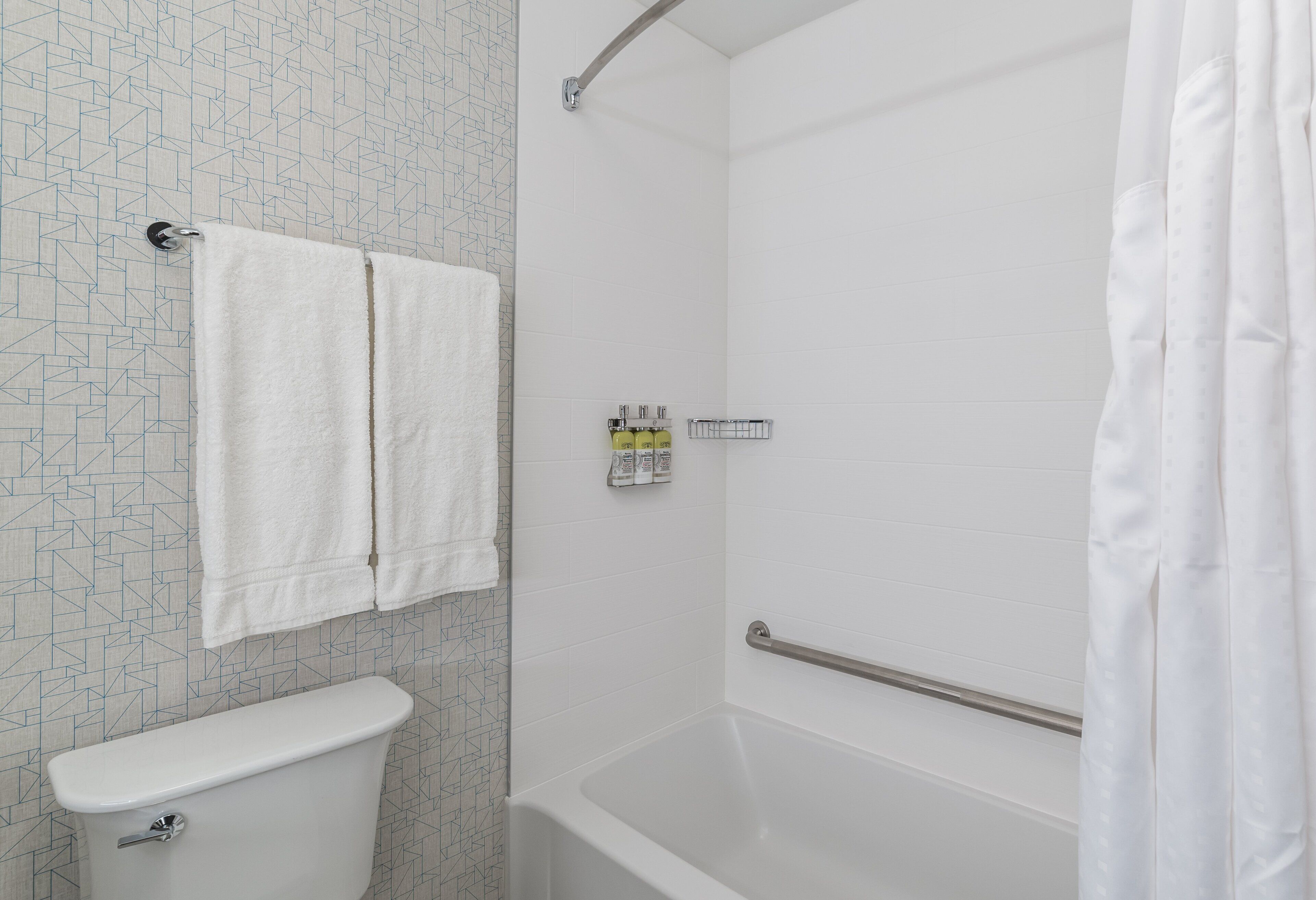 Une salle de bain comprenant des toilettes, une douche équipée d’une barre d’appui et un porte-serviettes.