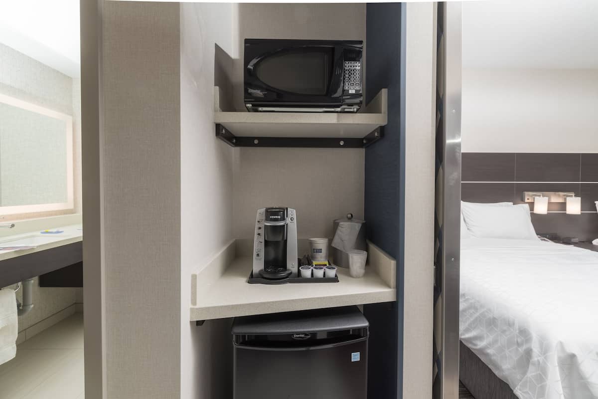 Habitación de hotel con kitchenette que incluye microondas, cafetera y contenedores de almacenamiento.