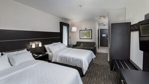 Une chambre d’hôtel avec deux lits, un bureau, une chaise, une télévision et un tableau encadré au mur.