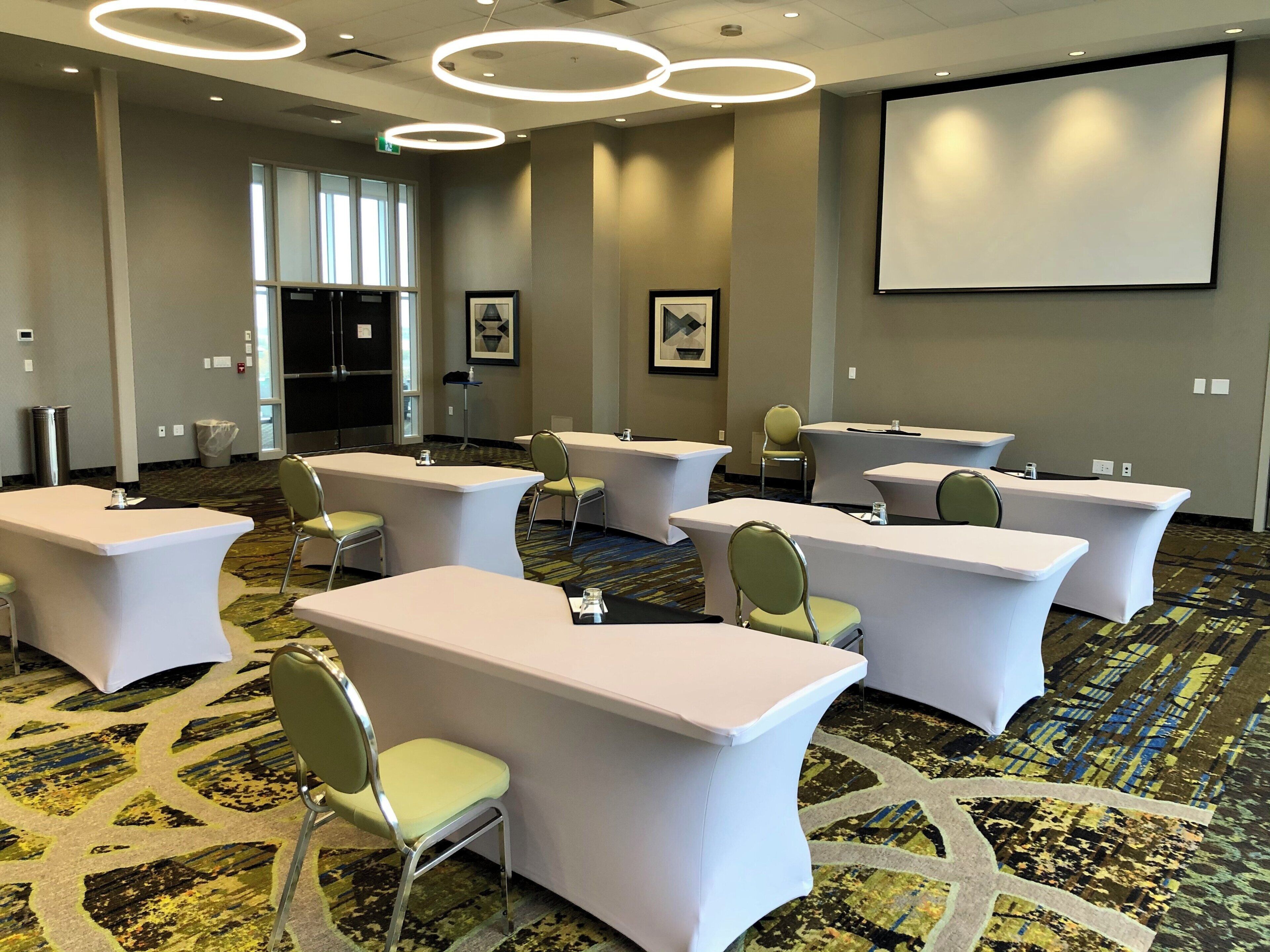 A conference room with multiple tables and chairs, a projector screen, and a patterned carpet.