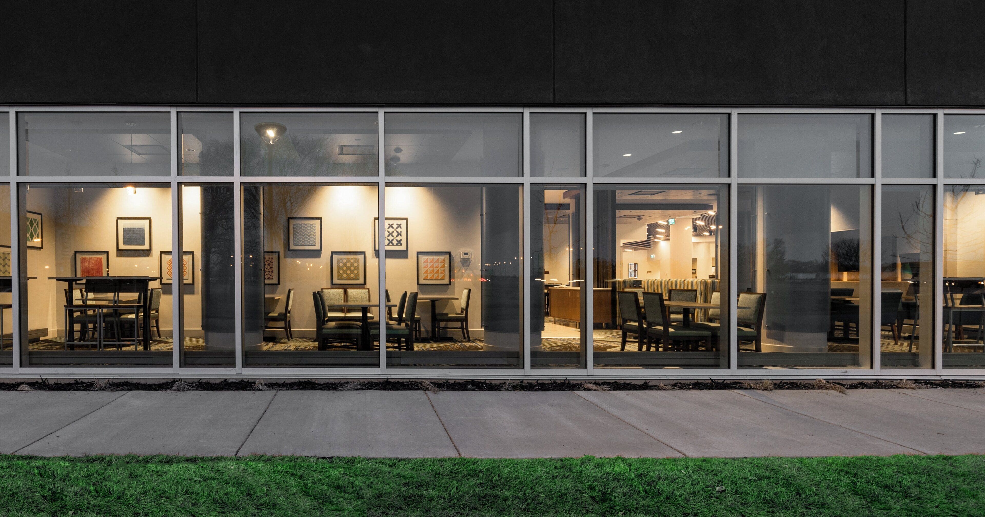 A modern building with large windows, a dining area with tables and chairs, and framed artwork on the walls.
