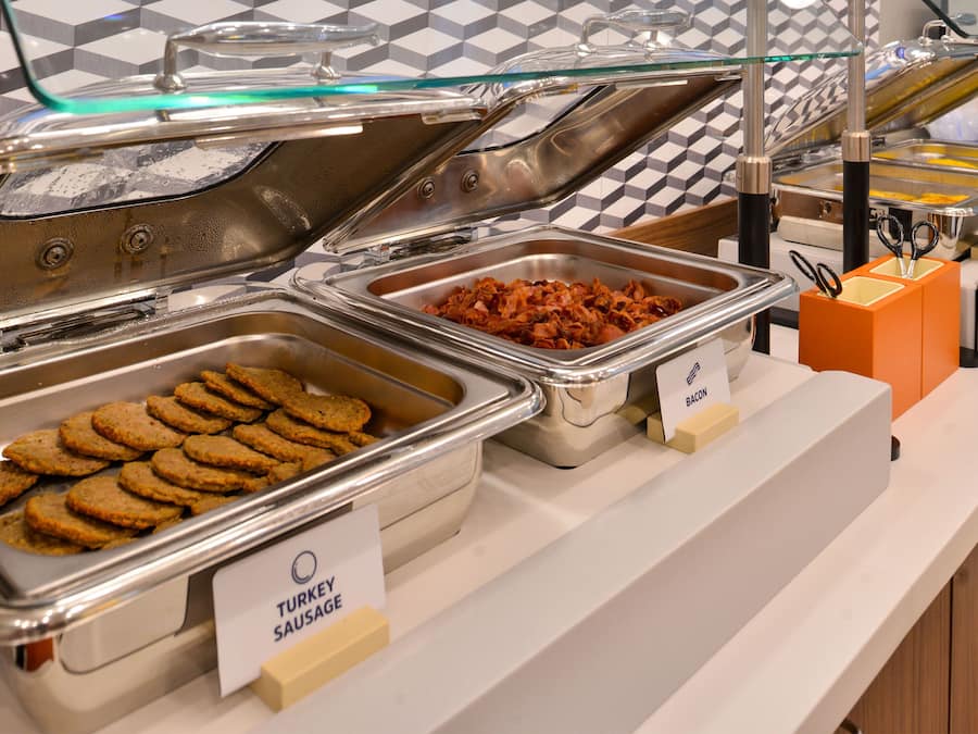 A buffet with labeled trays of turkey sausage, bacon, and other items.