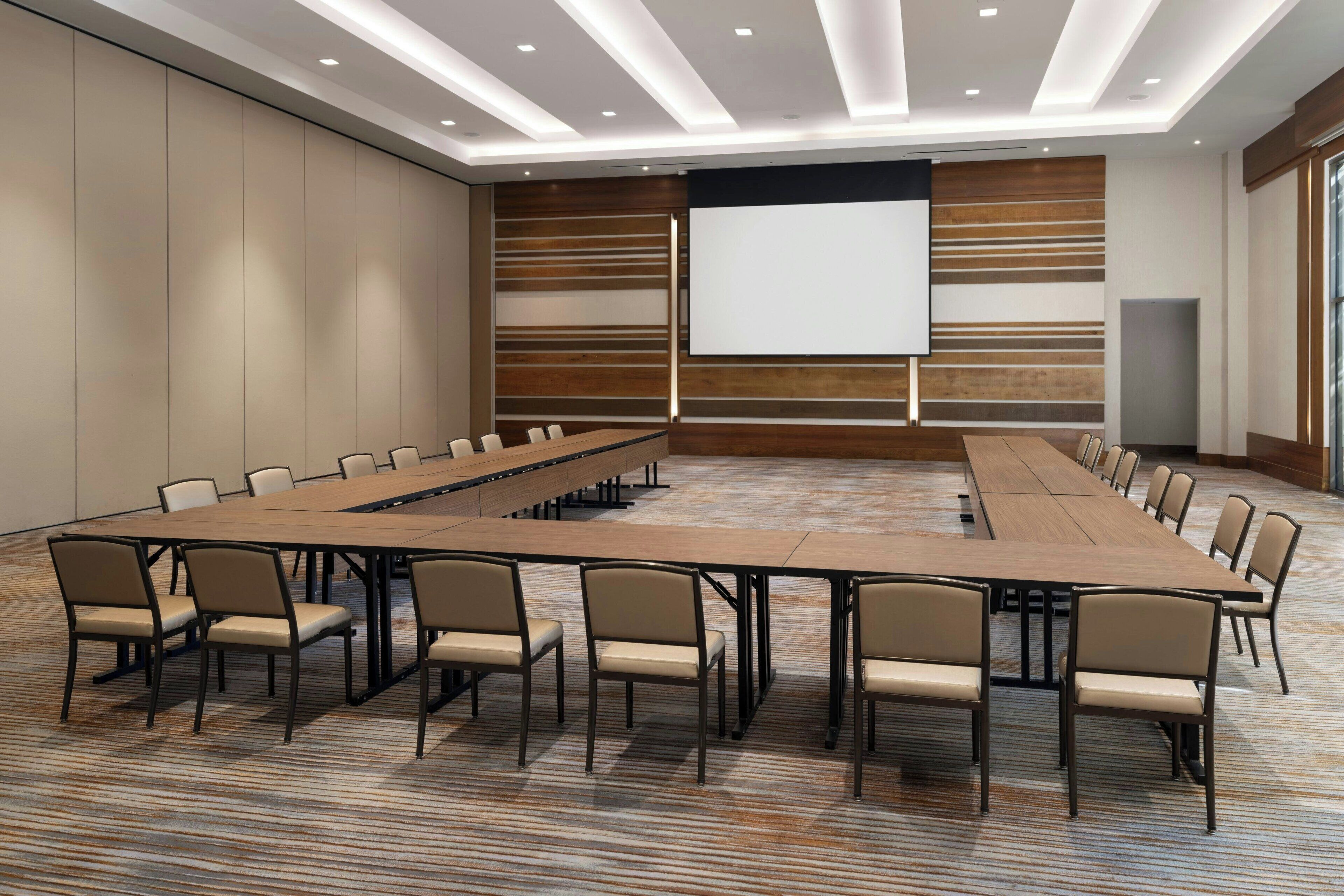 A conference room with a long table, multiple chairs, a projector screen, and a large window.