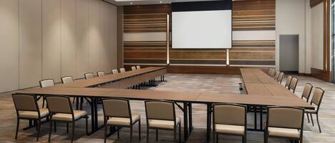 A conference room with a long table, multiple chairs, a projector screen, and a large window.