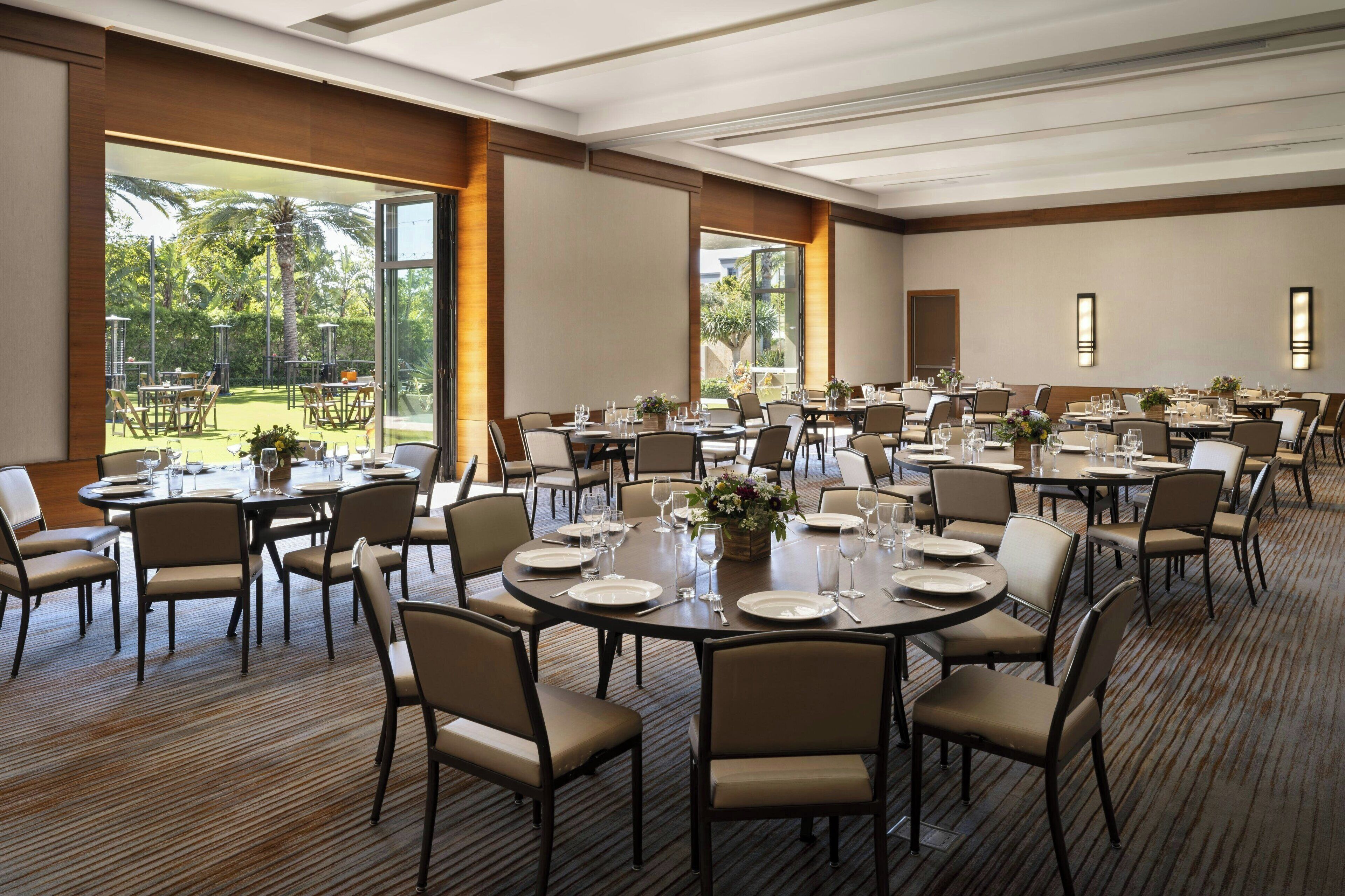 A conference room with round tables, chairs, and a large window overlooking a garden.
