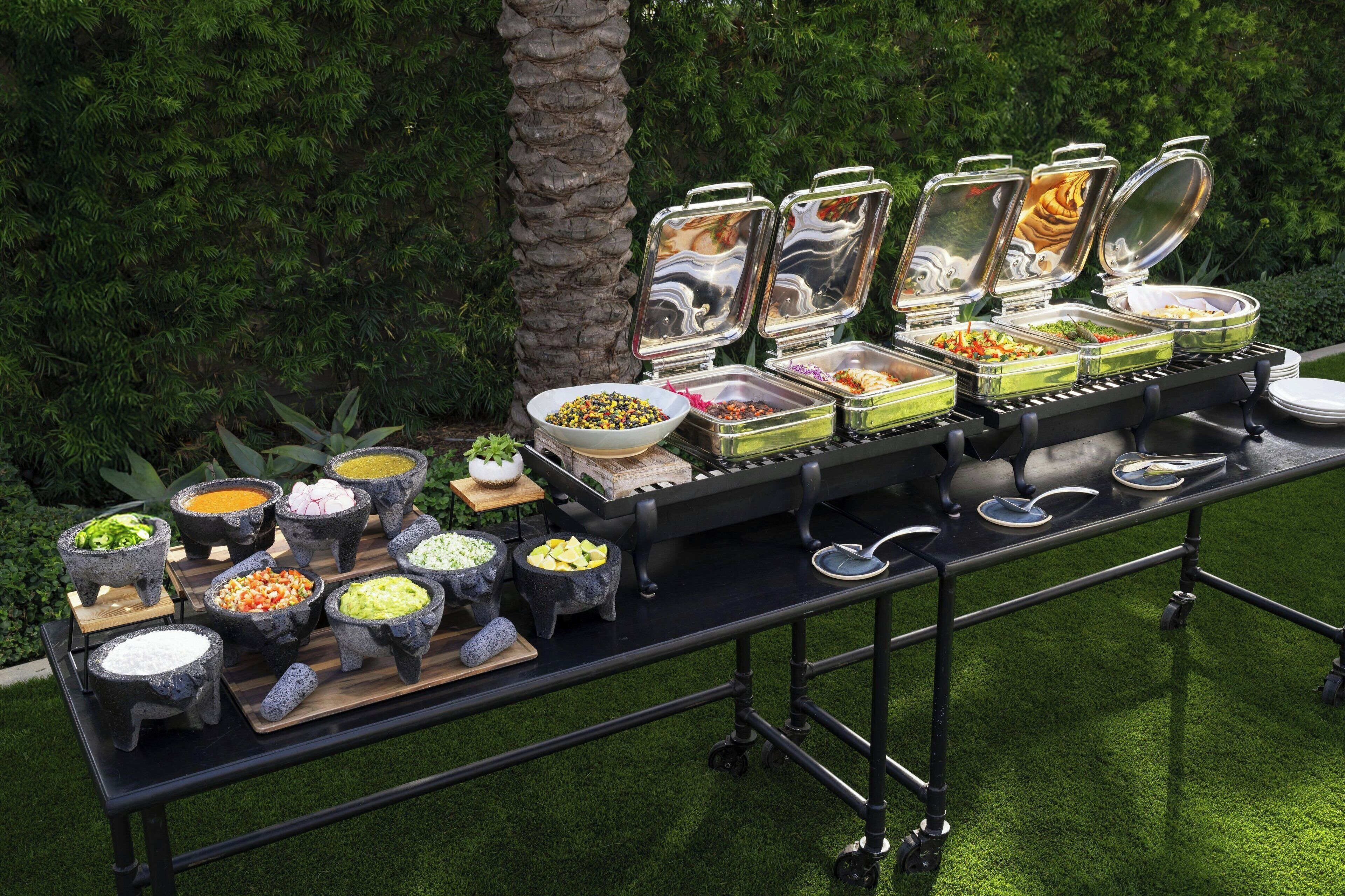 Una mesa de buffet con diferentes recipientes de comida y una palmera al fondo.