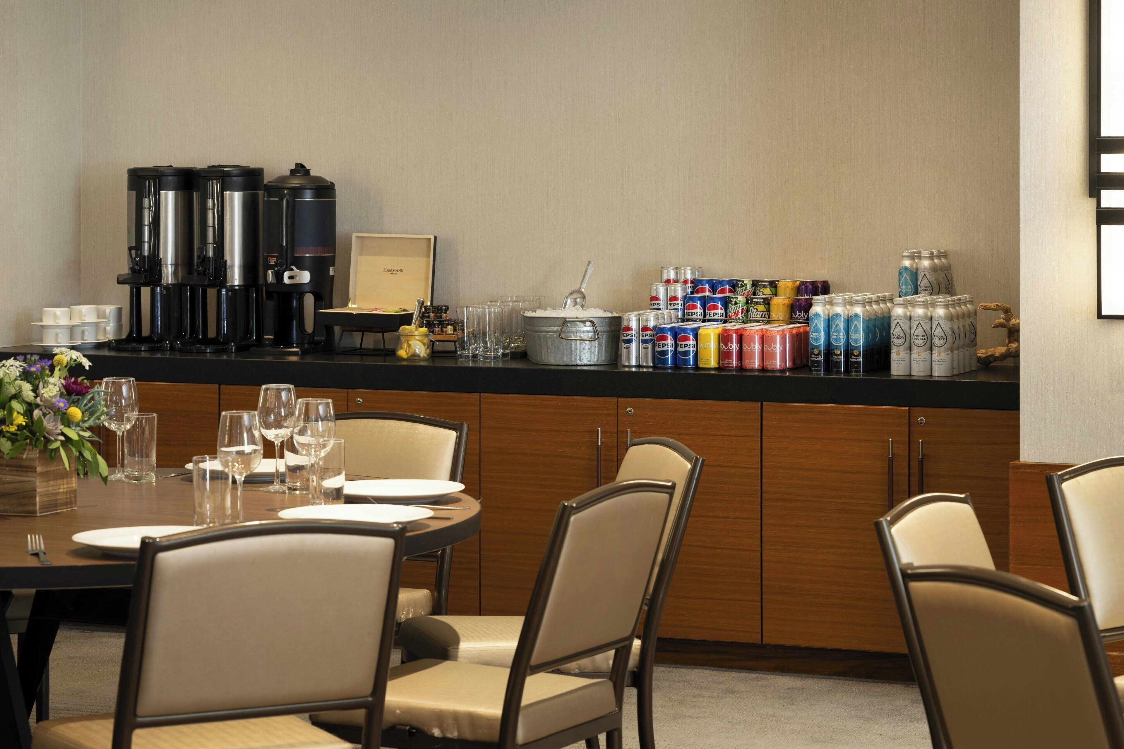 A hotel dining area with a counter, coffee machines, and beverage dispensers.