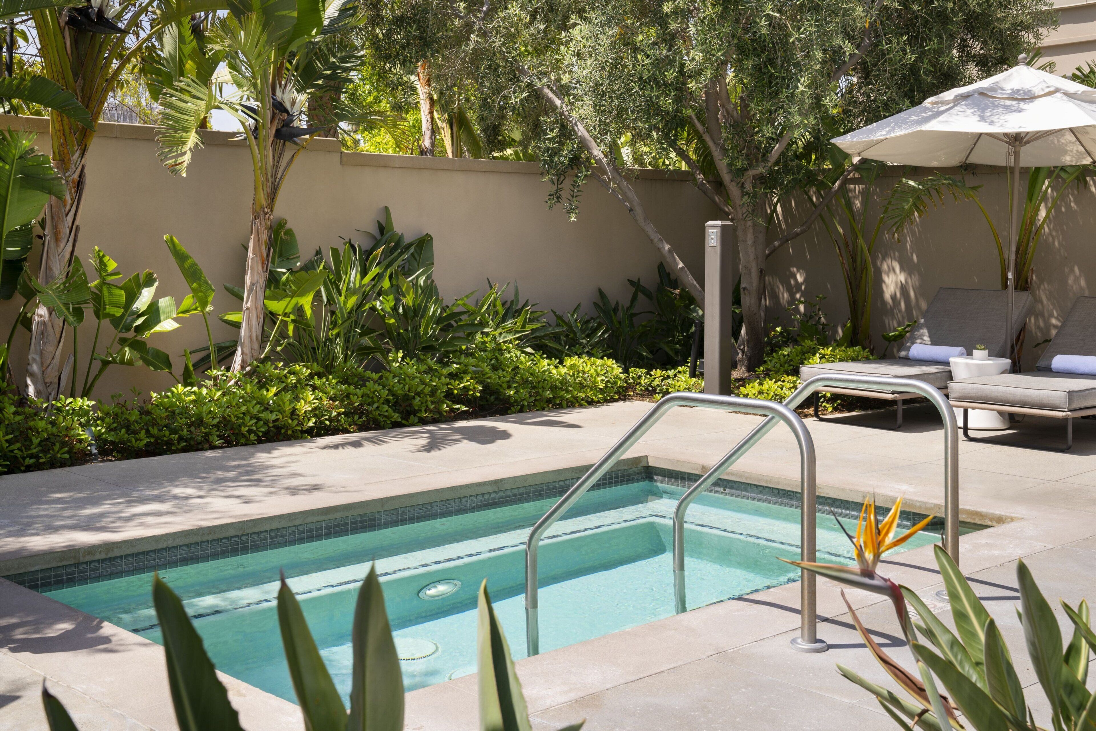 A pool area with a metal ladder, lounge chairs, and an umbrella.