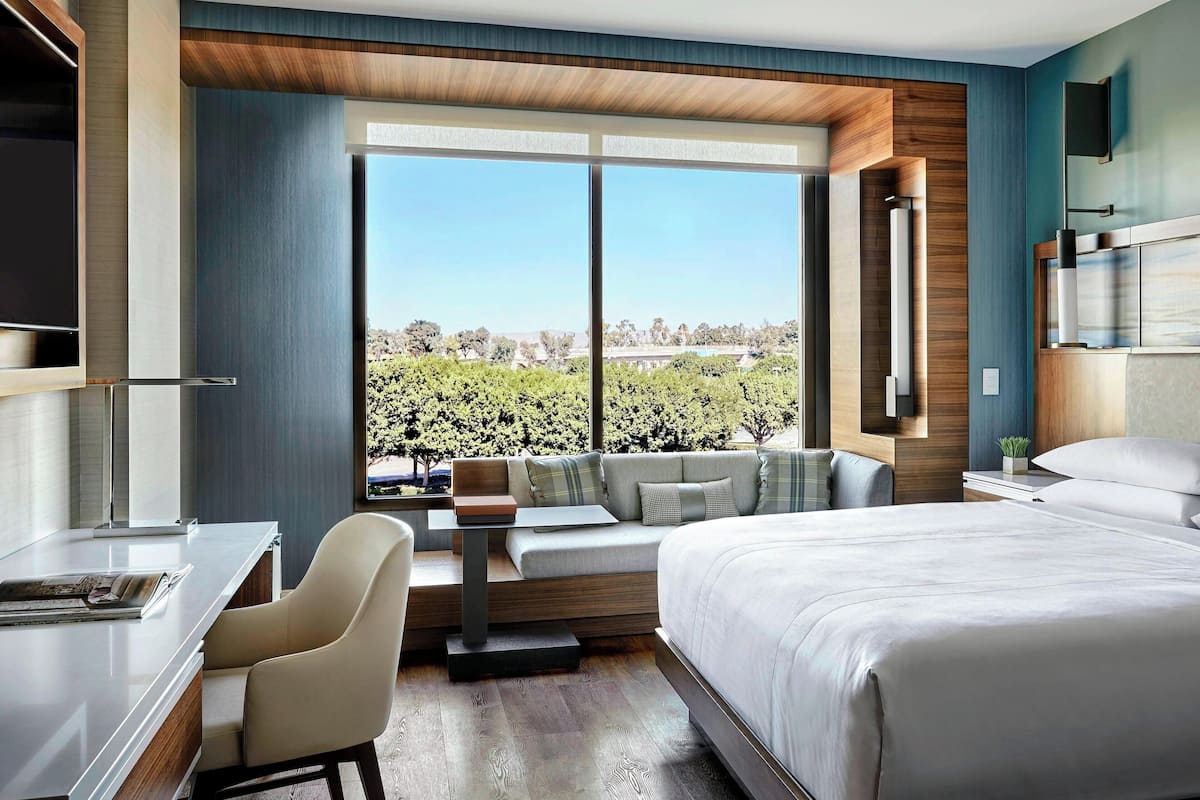 A modern hotel room with a large bed, a desk, and a seating area by the window.