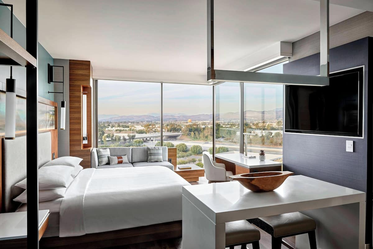 A modern hotel room with a large bed, a desk, and a view of the cityscape.