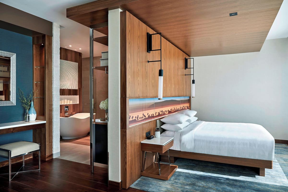 A modern hotel room with a wooden ceiling, a large bed, a desk, and a bathroom with a bathtub.