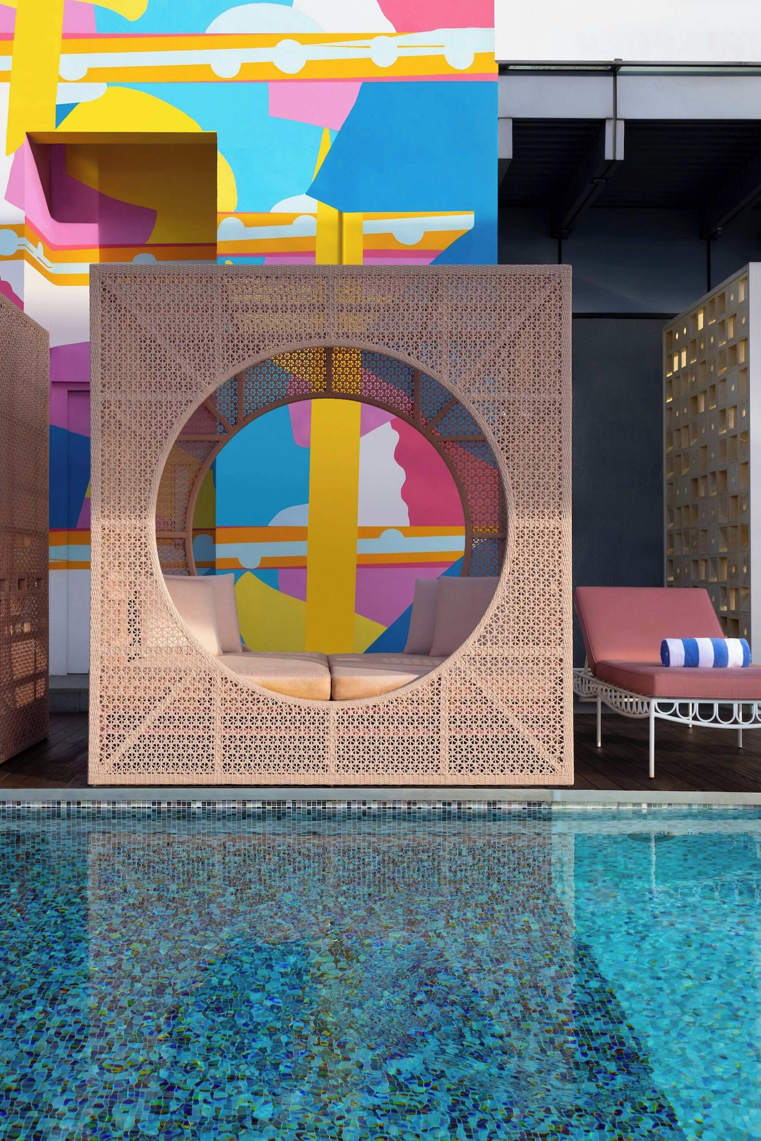 Zona de piscina con una estructura de asientos circular, una silla de descanso y un mural colorido al fondo.