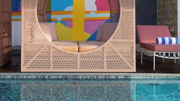 Zona de piscina con una estructura de asientos circular, una silla de descanso y un mural colorido al fondo.