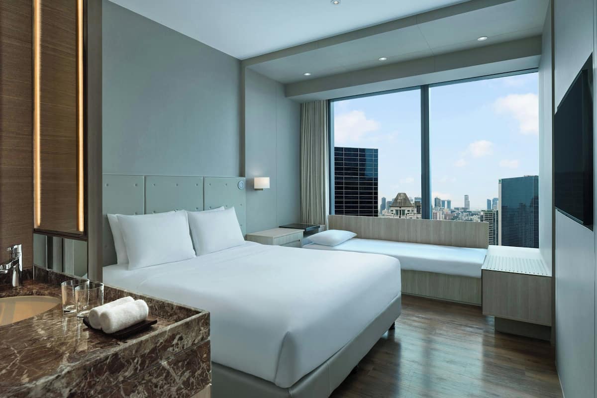 A modern hotel room with a large bed, a seating area by the window, a marble bathroom, and a city view.