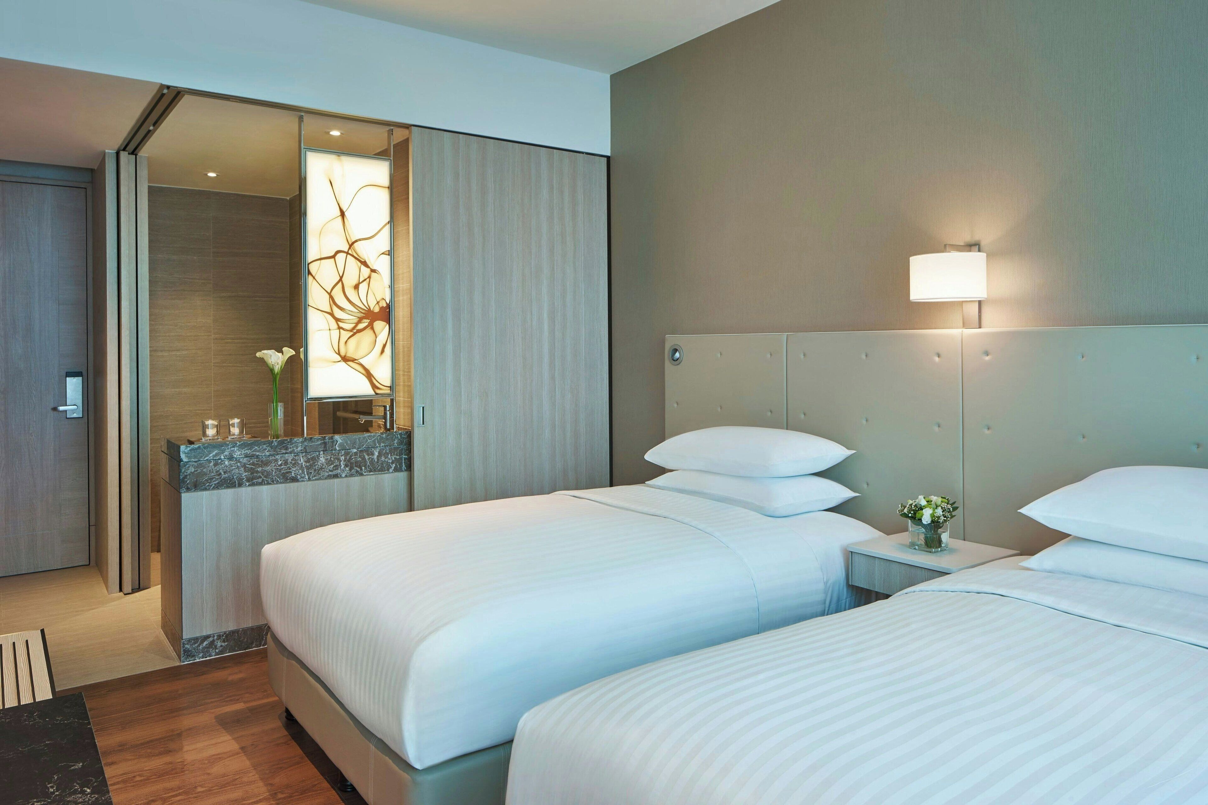 A hotel room with two beds, a bathroom, and a small sitting area.