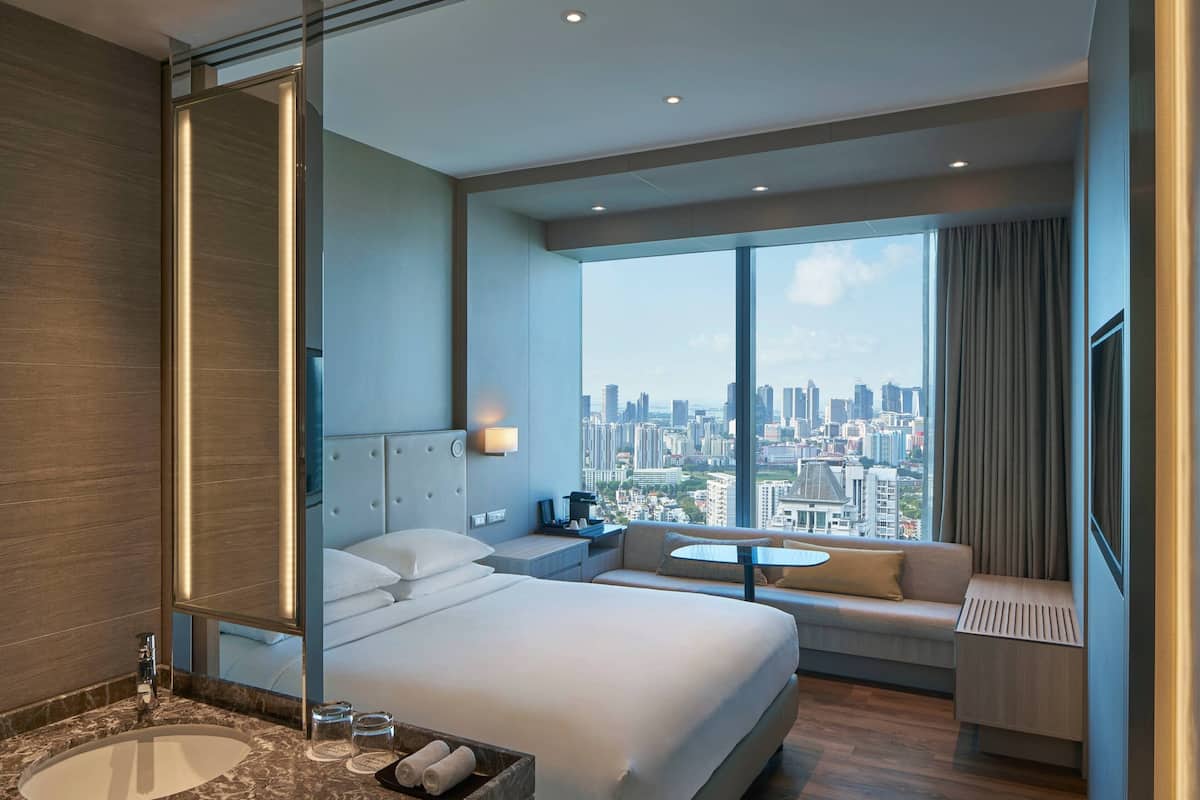 Ein modernes Hotelzimmer mit einem großen Bett, einer Sitzecke, einem kleinen Tisch und Blick auf die Stadt.