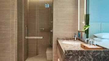 Un baño moderno con ducha envuelta en vidrio, encimeras de mármol y un espejo grande.