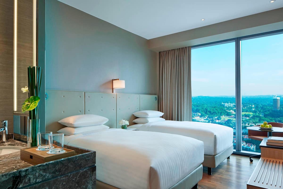 Ein modernes Hotelzimmer mit zwei Betten, einem großen Fenster mit Blick auf die Stadt, einem Badezimmer mit Marmorplatte und einer Essecke mit Tisch und Stühlen.