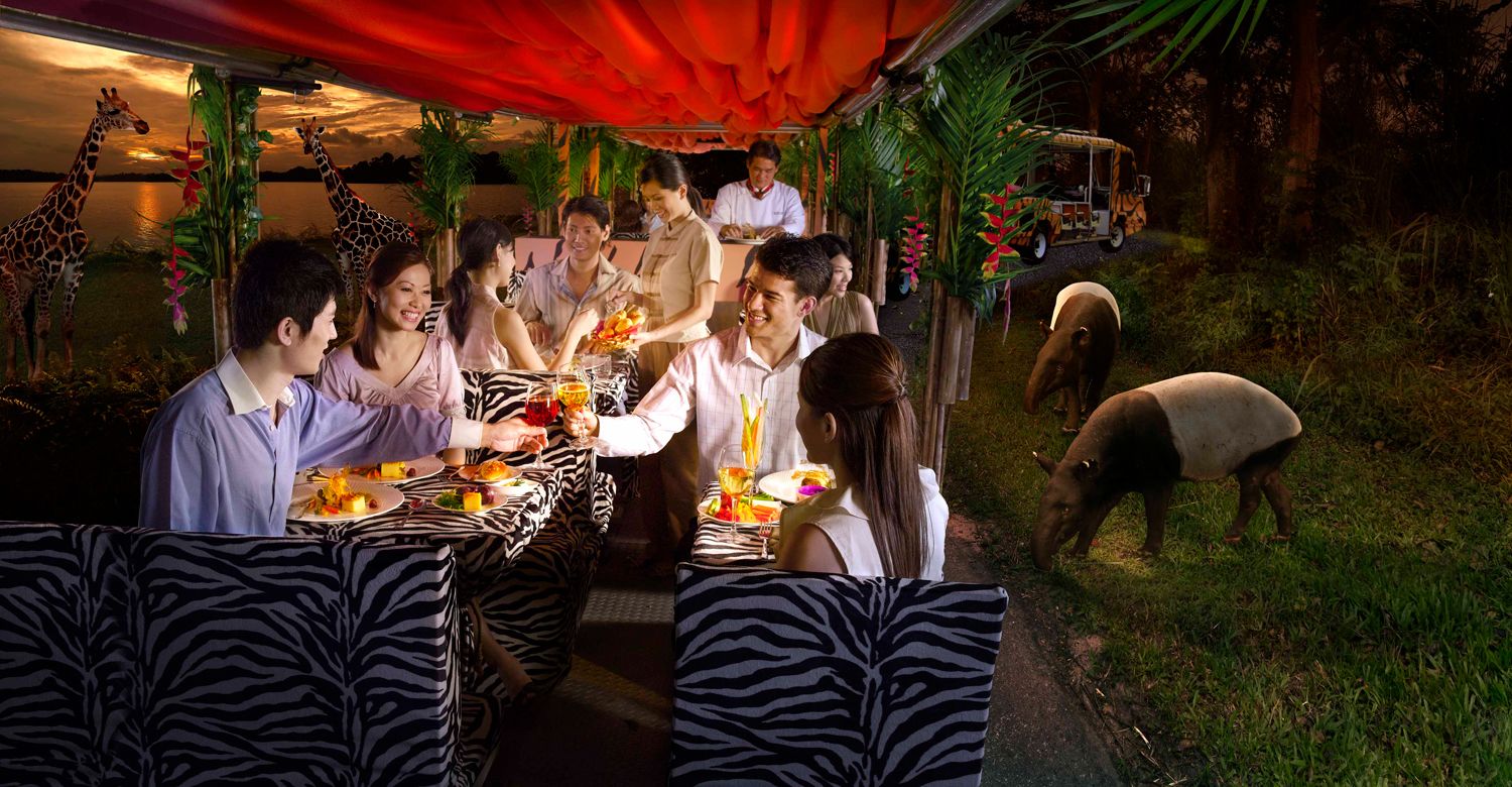 A group dining outdoors with zebra-patterned furniture, a red canopy, and a giraffe statue.