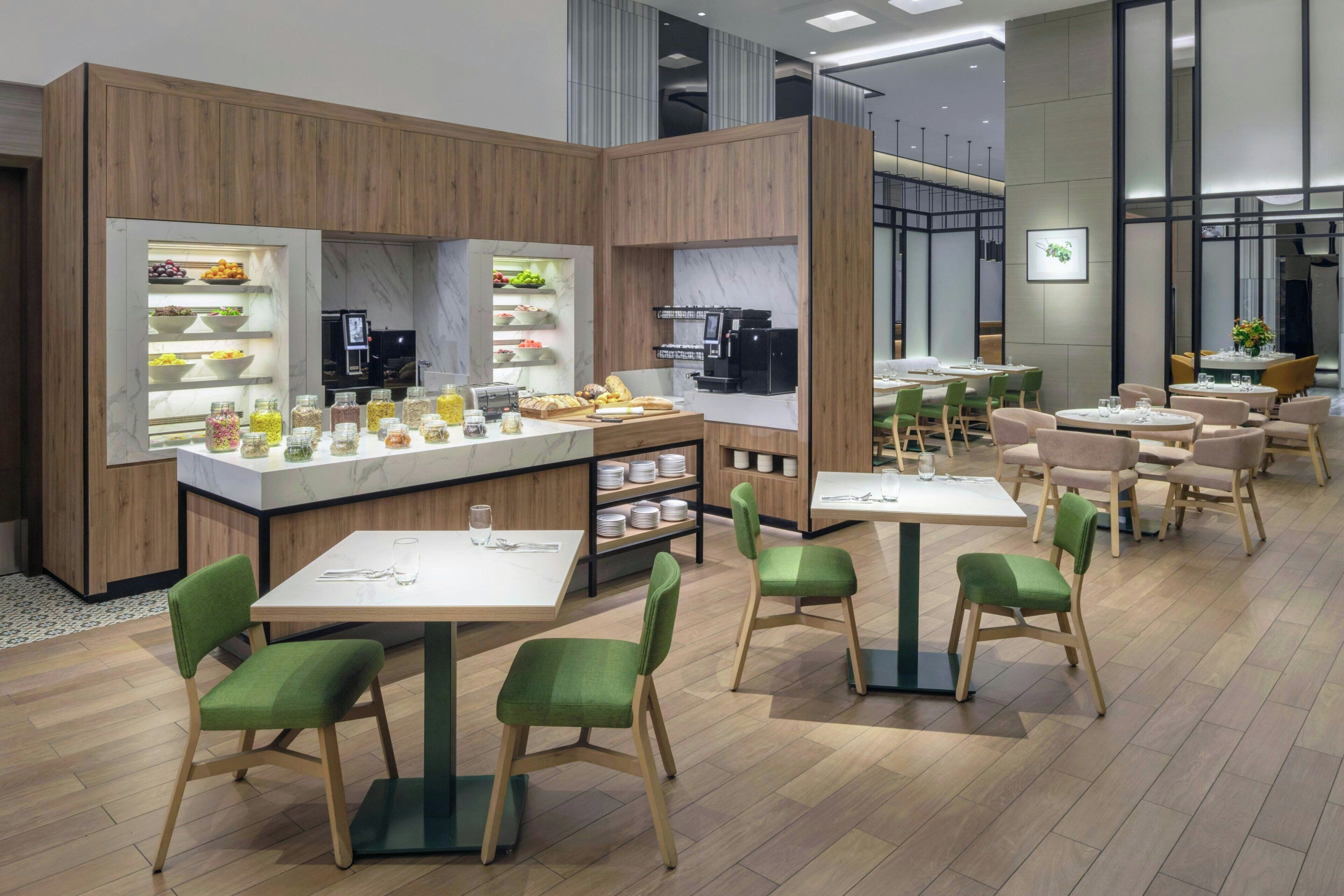 Una cafetería moderna con divisiones de madera, mostradores de mármol y sillas tapizadas en verde.