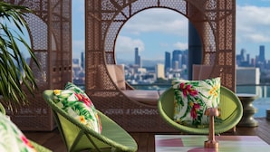 Un salon sur le toit, avec des fauteuils en osier, une arche décorative et une vue sur les toits de la ville.