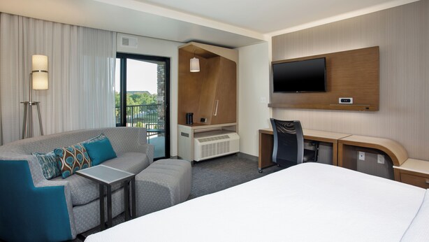 A modern hotel room with a large bed, a sofa, a desk, and a TV mounted on the wall. - Courtyard by Marriott Dallas Flower Mound (Flower Mound)