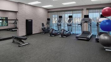 A gym with treadmills, elliptical machines, a bench press, and exercise balls.