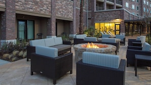 An outdoor patio area with wicker furniture, a stone fire pit, and a building entrance in the background. - Courtyard by Marriott Dallas Flower Mound (Flower Mound)