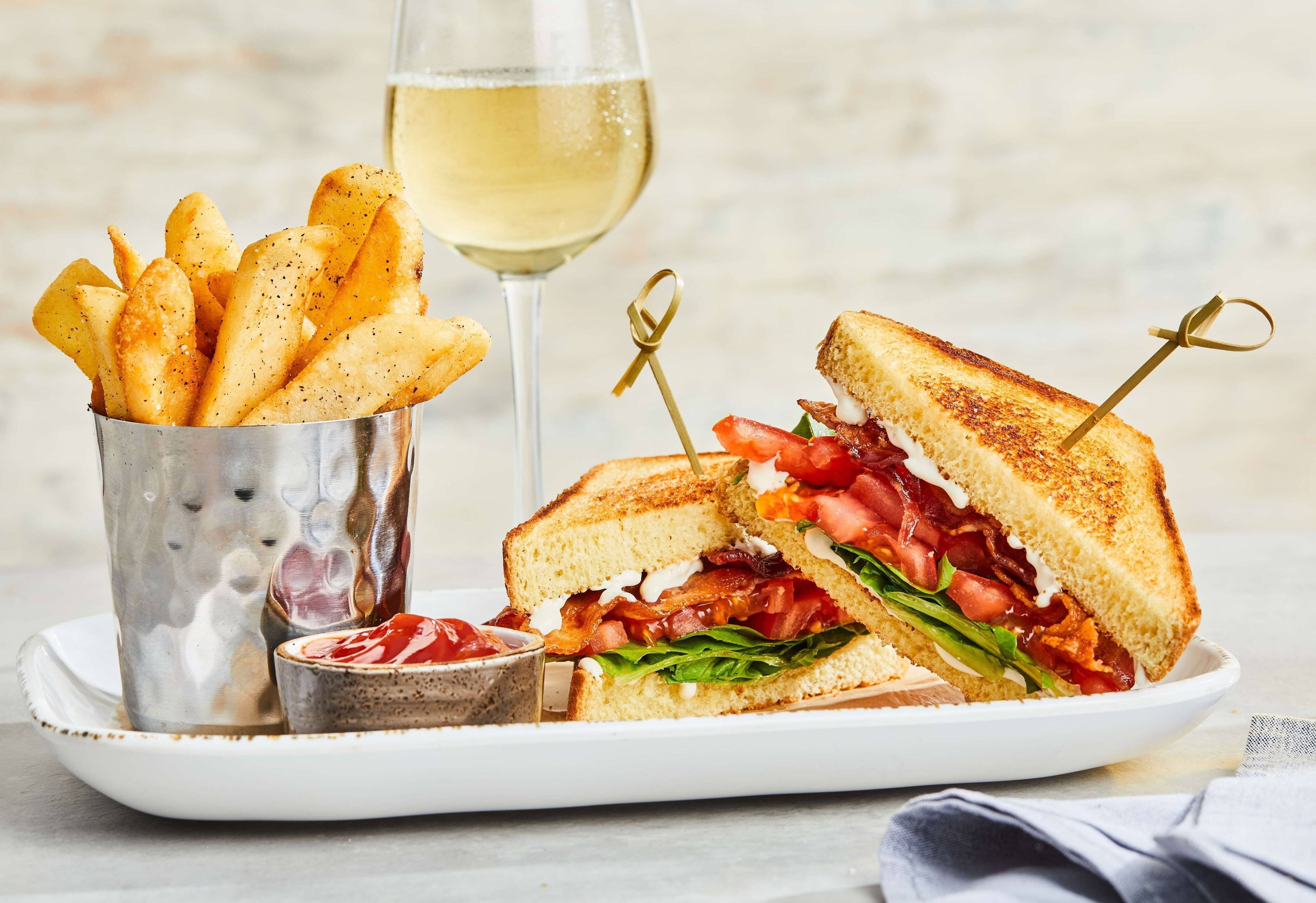 A sandwich with a side of fries and a glass of white wine.