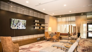 A modern lobby with a large flat-screen TV, comfortable seating, a reception desk, and a decorative wall with shelves. - Courtyard by Marriott Dallas Flower Mound (Flower Mound)