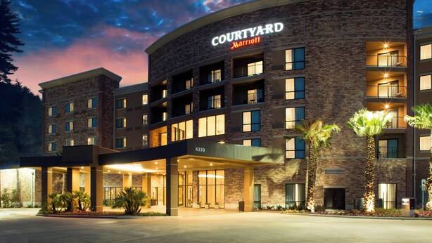 A Courtyard Marriott hotel with a brick facade, multiple balconies, and a covered entrance area. - Courtyard by Marriott Dallas Flower Mound (Flower Mound)