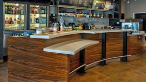 A modern bar area with wooden accents, a curved counter, and shelves stocked with bottles and glasses. - Courtyard by Marriott Dallas Flower Mound (Flower Mound)