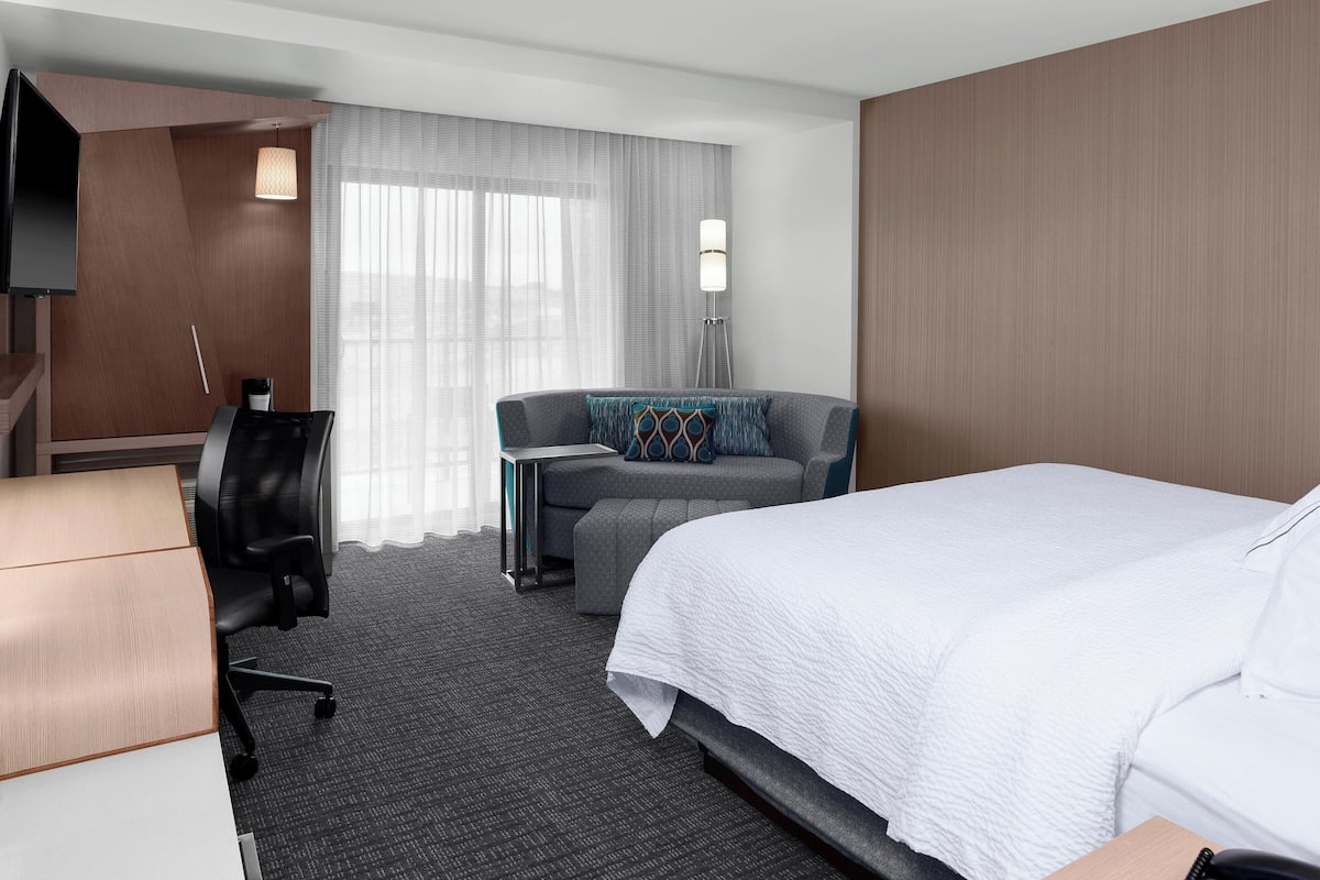 A hotel room with a bed, a desk, a chair, a sofa, and a TV.