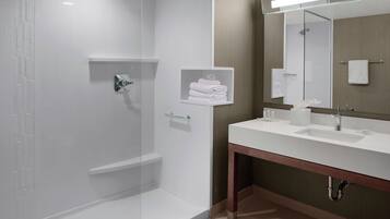 A modern bathroom with a glass-enclosed shower, a vanity with a mirror, and neatly folded towels on a shelf.