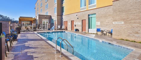 A swimming pool with lounge chairs and a 'NO DIVING' sign, surrounded by a building with multiple windows and a brick facade.