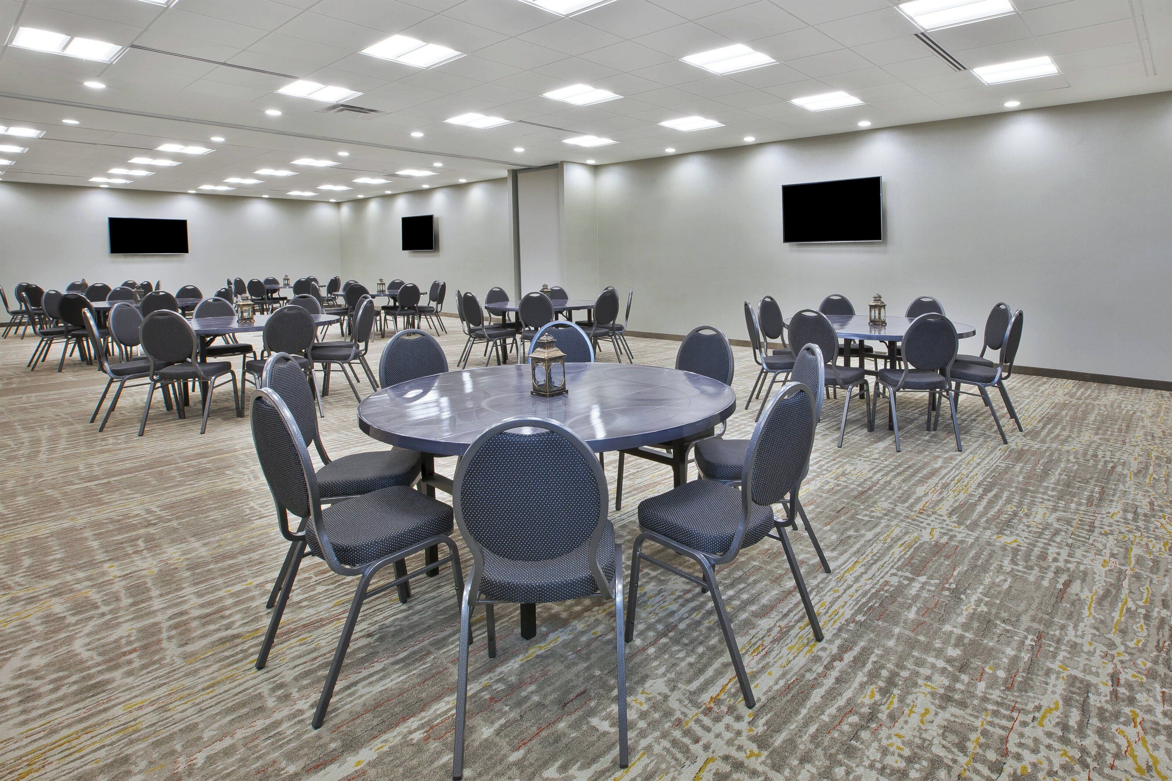 A conference room with round tables, chairs, a carpeted floor, and ceiling lights.